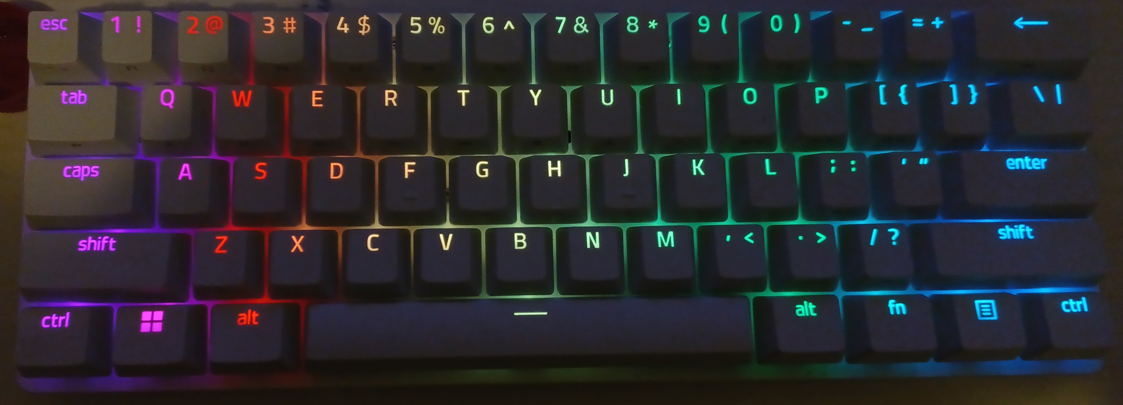 a photo of a razer huntsman mini keyboard, in white with RGB backlighting. the photo is dark to accentuate the color of the lights.