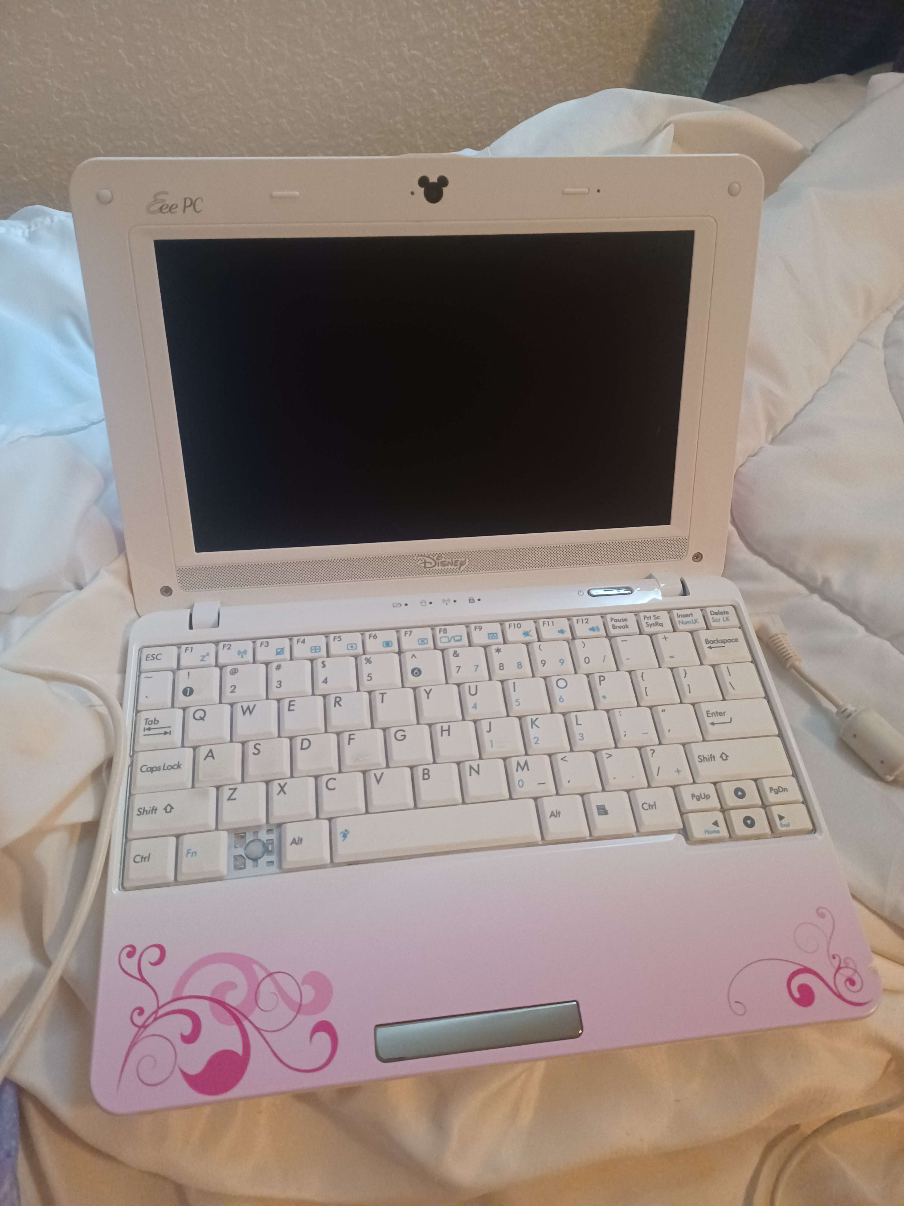 a photo of a netbook -- specifically a disney-themed asus EEEPC -- open but not turned on. it is pink with a white keyboard.